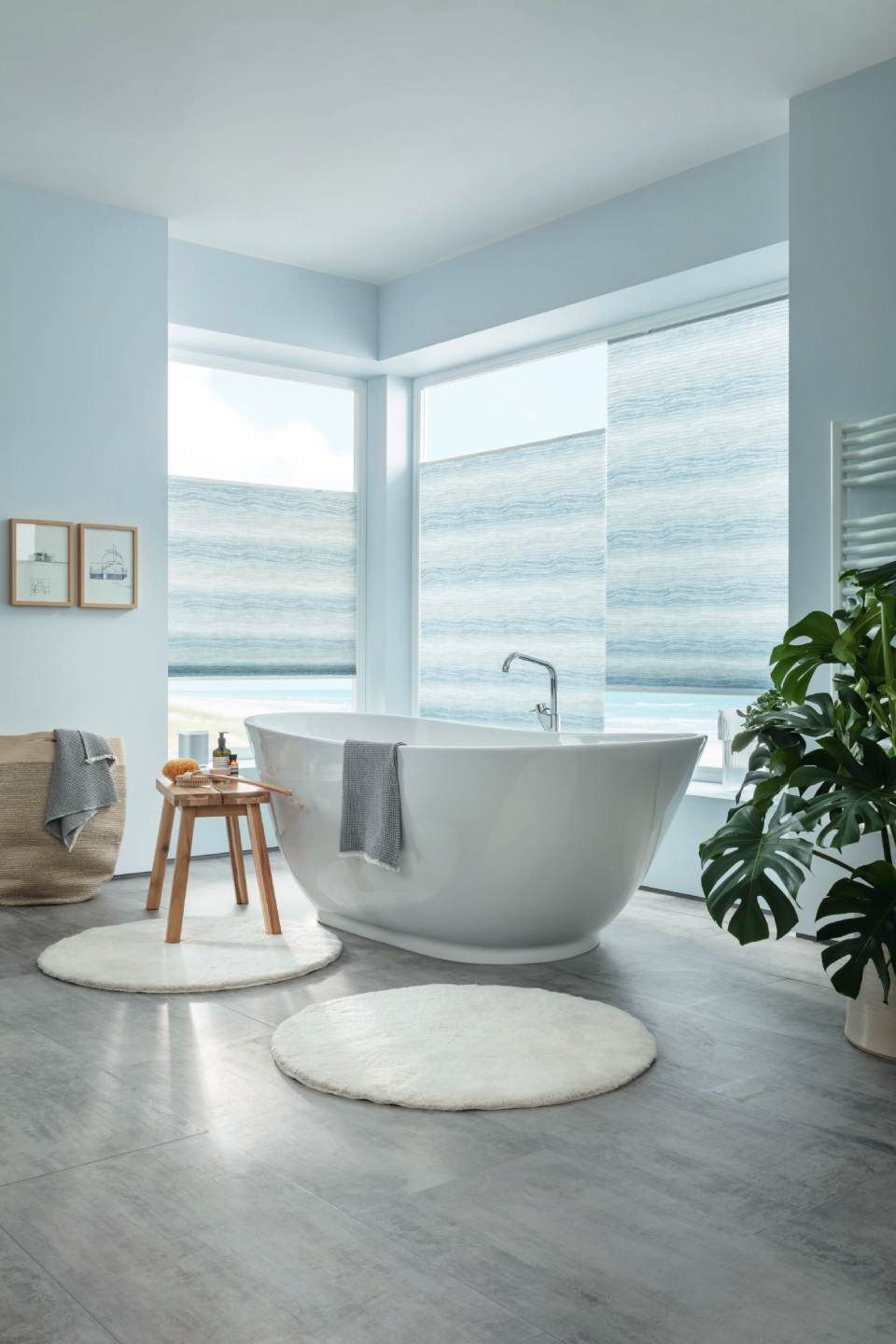 Badezimmer mit weißer Badewanne, runden Teppichen und großen Fenstern mit Jalousien.