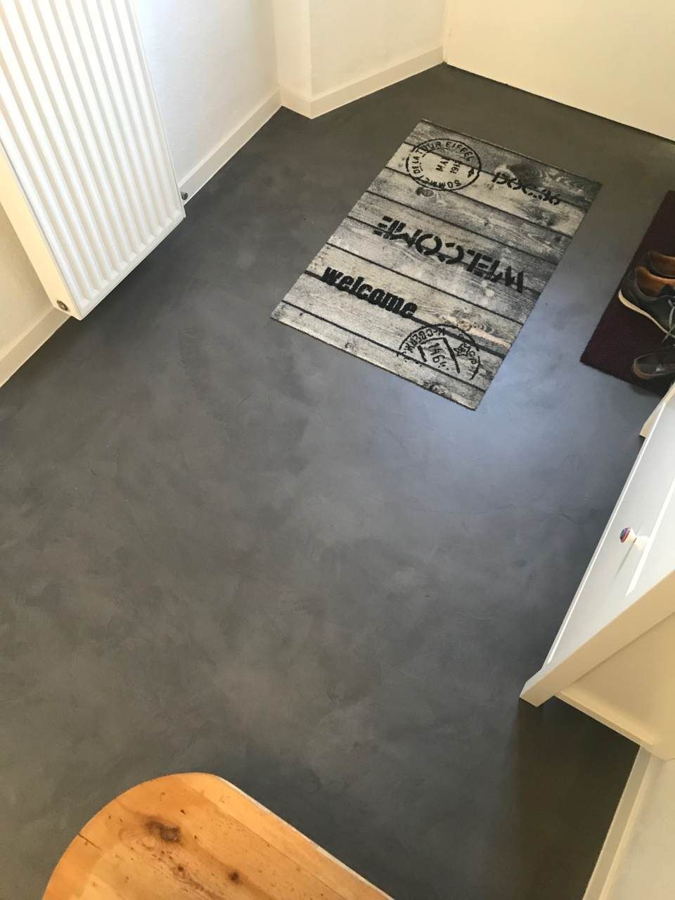 Eingangsbereich mit grauem Boden, Fußmatte und weißem Heizkörper.