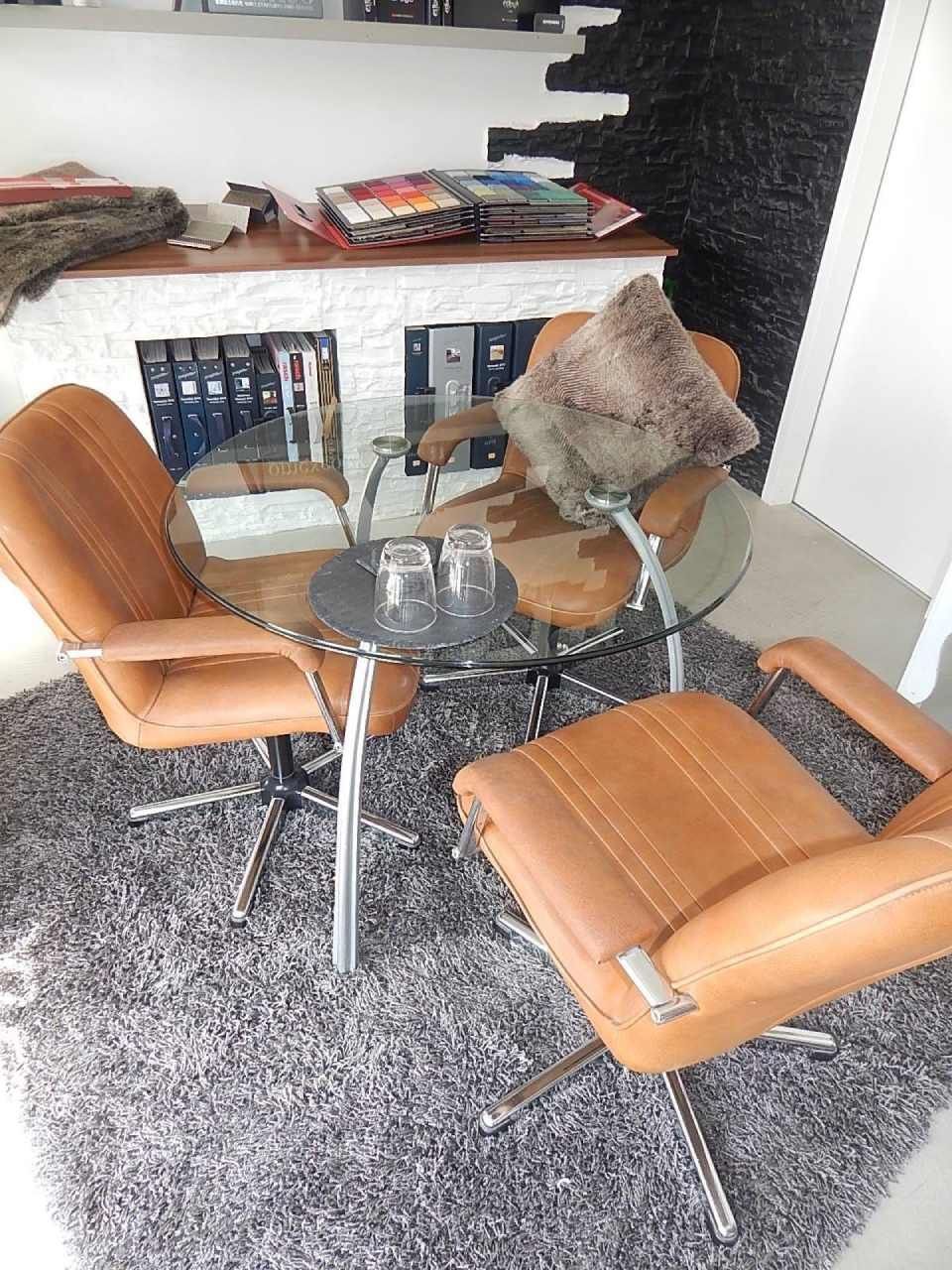 Runder Glastisch mit zwei hellbraunen Lederstühlen, Teppich und dekorativem Kissen.