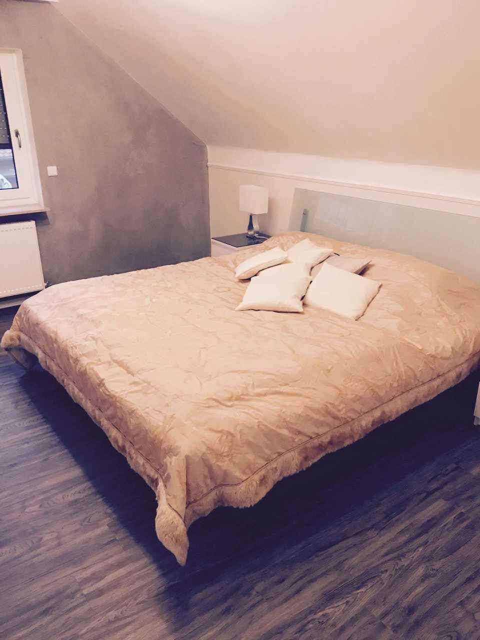 Schlafzimmer mit einem großen Bett, bedeckt mit einer hellbraunen Decke und Kissen.