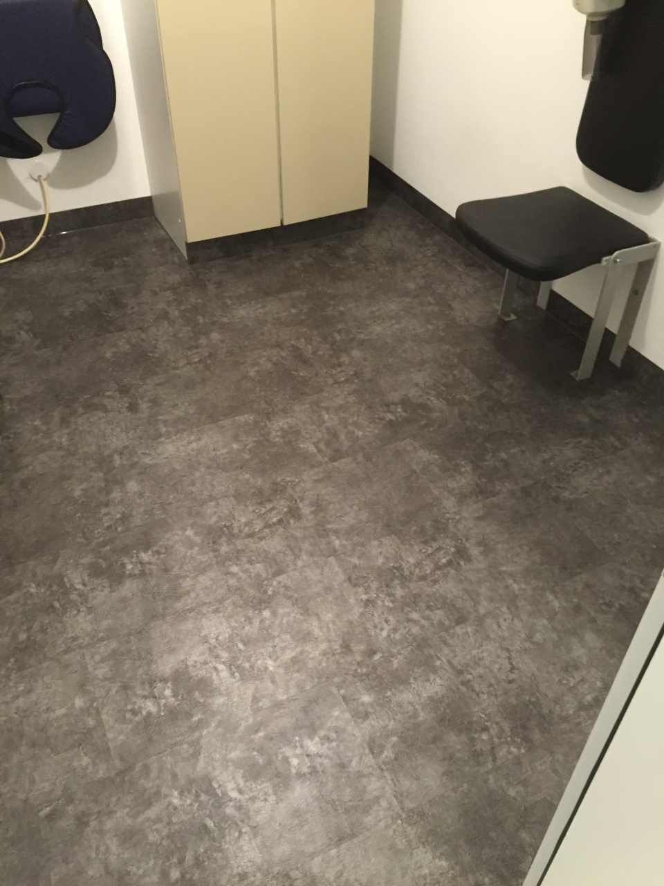 Dunkelgrauer strukturierter Boden in einem Raum mit weißen Wänden, einem Schrank und einem Stuhl.