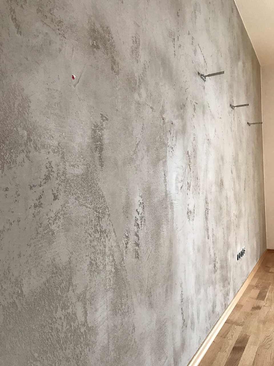 Strukturierte graue Wand mit eingebetteten Montagehalterungen, Holzboden an der Basis.