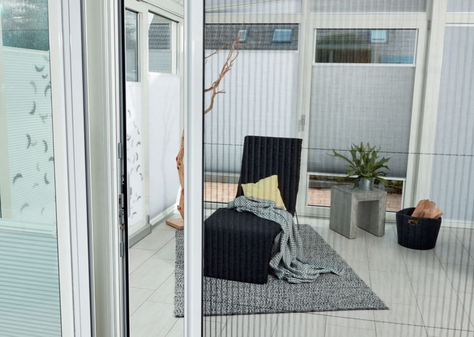 Wintergarten-Innenraum mit Stuhl, Teppich, Pflanzen und Plissees.