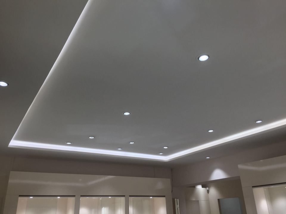 Weiße abgehängte Decke mit LED-Lichtbändern und Einbaustrahlern.