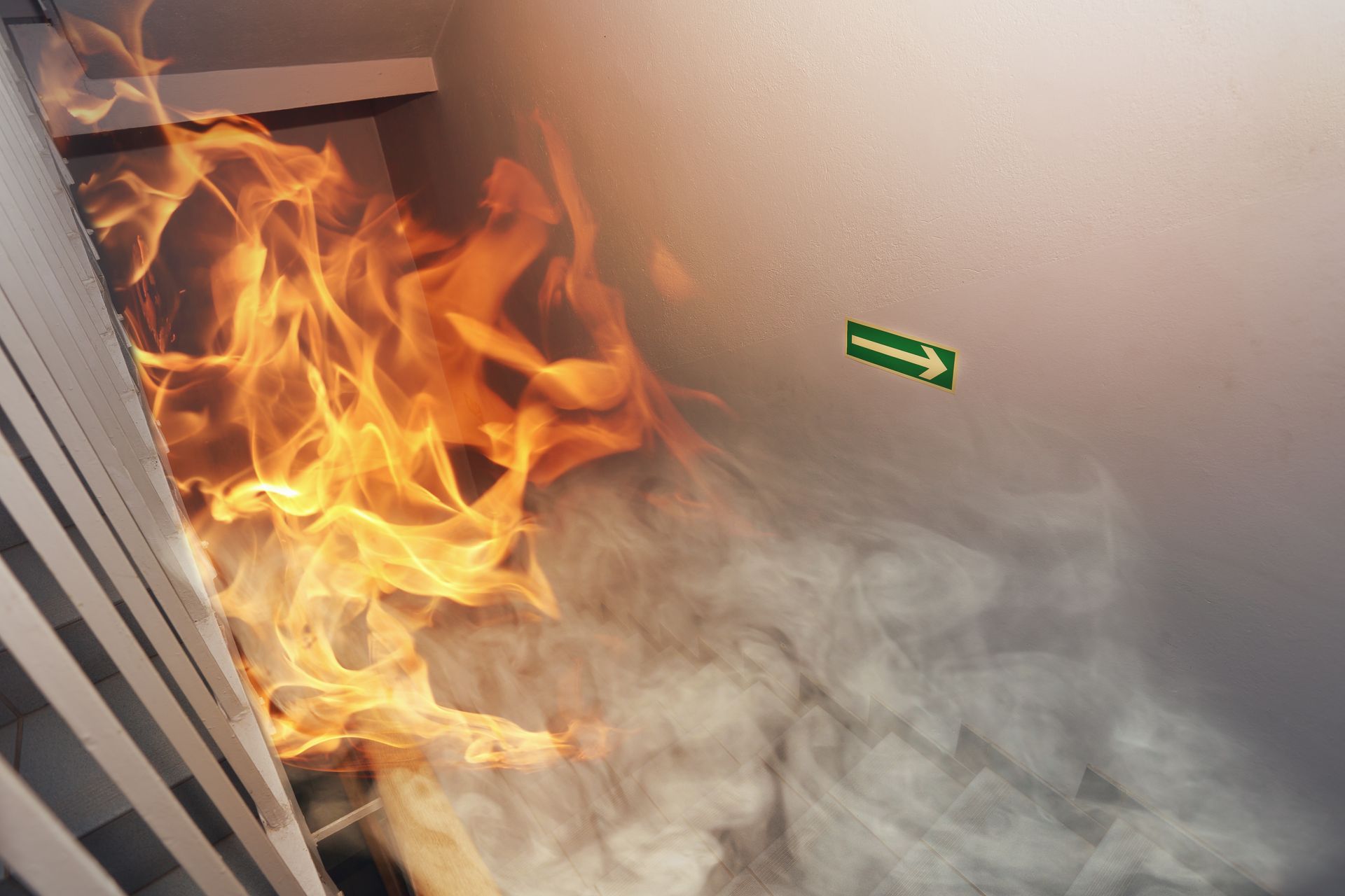 Un feu brûle contre un mur, dégageant une épaisse fumée, et un panneau de sortie vert est visible au-dessus.