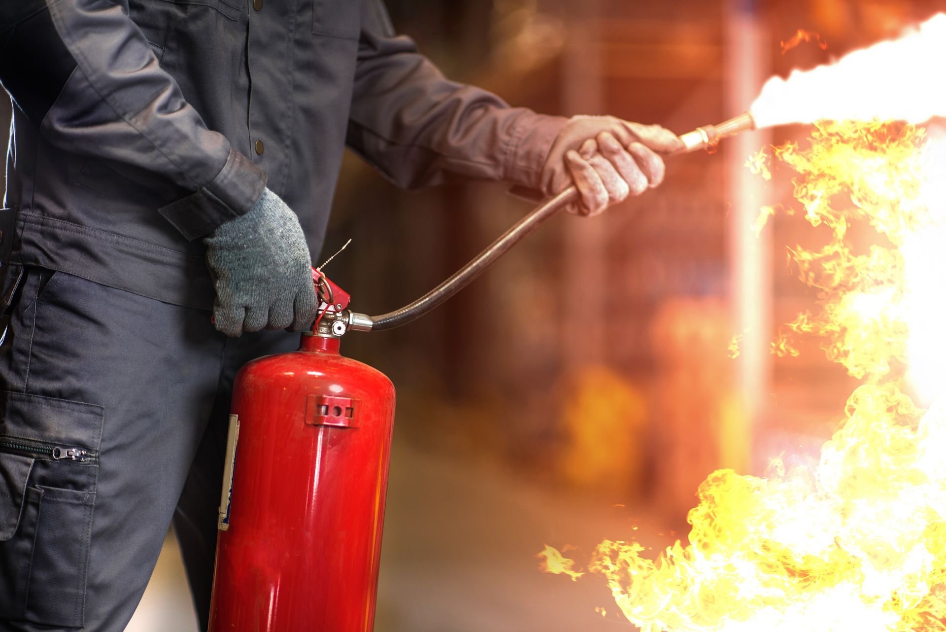 Une personne utilise un extincteur rouge pour éteindre un incendie à l'intérieur d'un bâtiment.