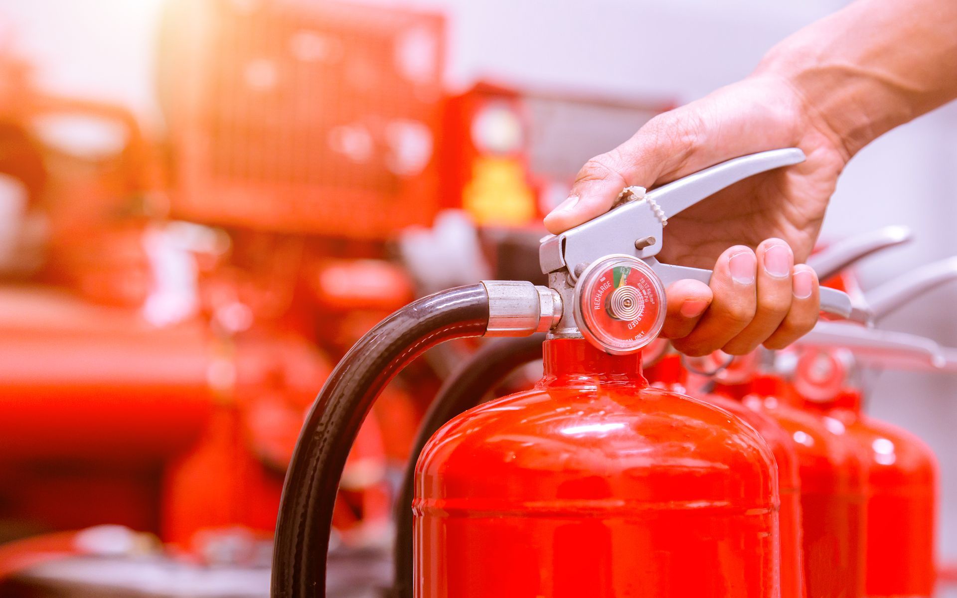 Main utilisant un tuyau d'extincteur près d'extincteurs rouges dans un environnement de sécurité incendie lumineux et flou.