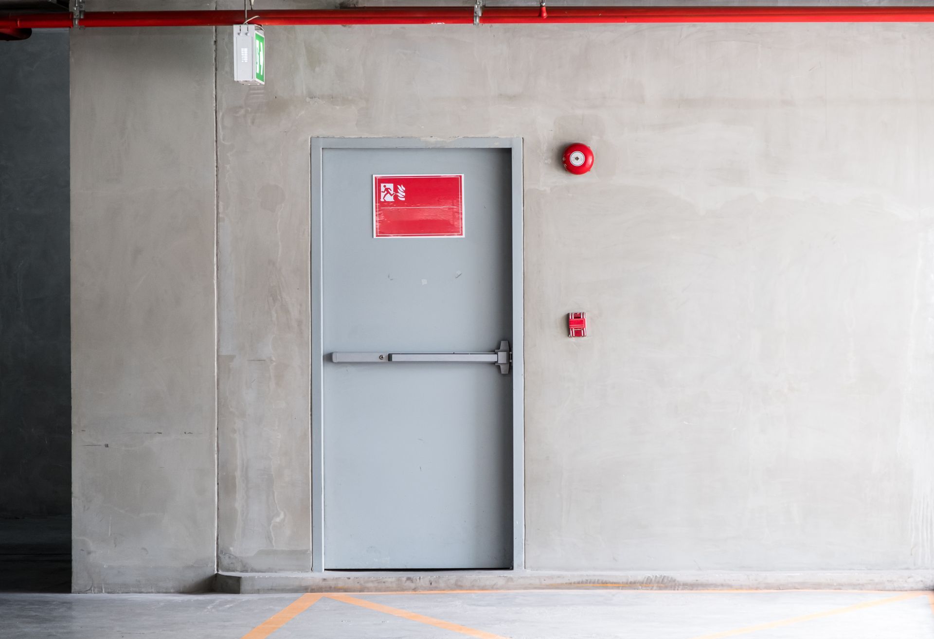 Porte métallique grise encastrée dans un mur en béton, avec des panneaux de sécurité rouges et un système d'alarme à proximité.
