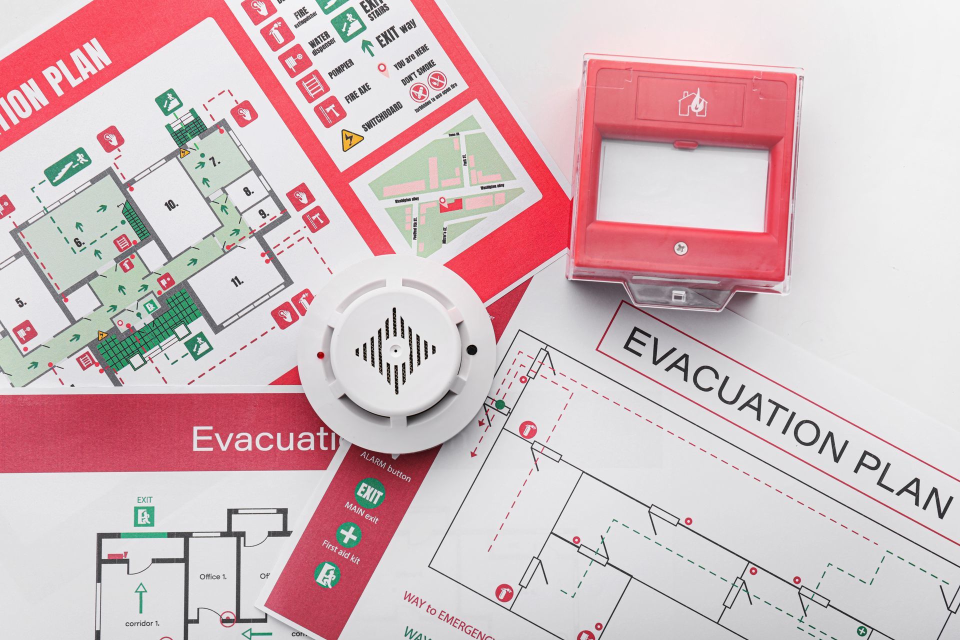 Des documents relatifs à l'alarme incendie, au détecteur de fumée et au plan d'évacuation se trouvent sur un bureau blanc.