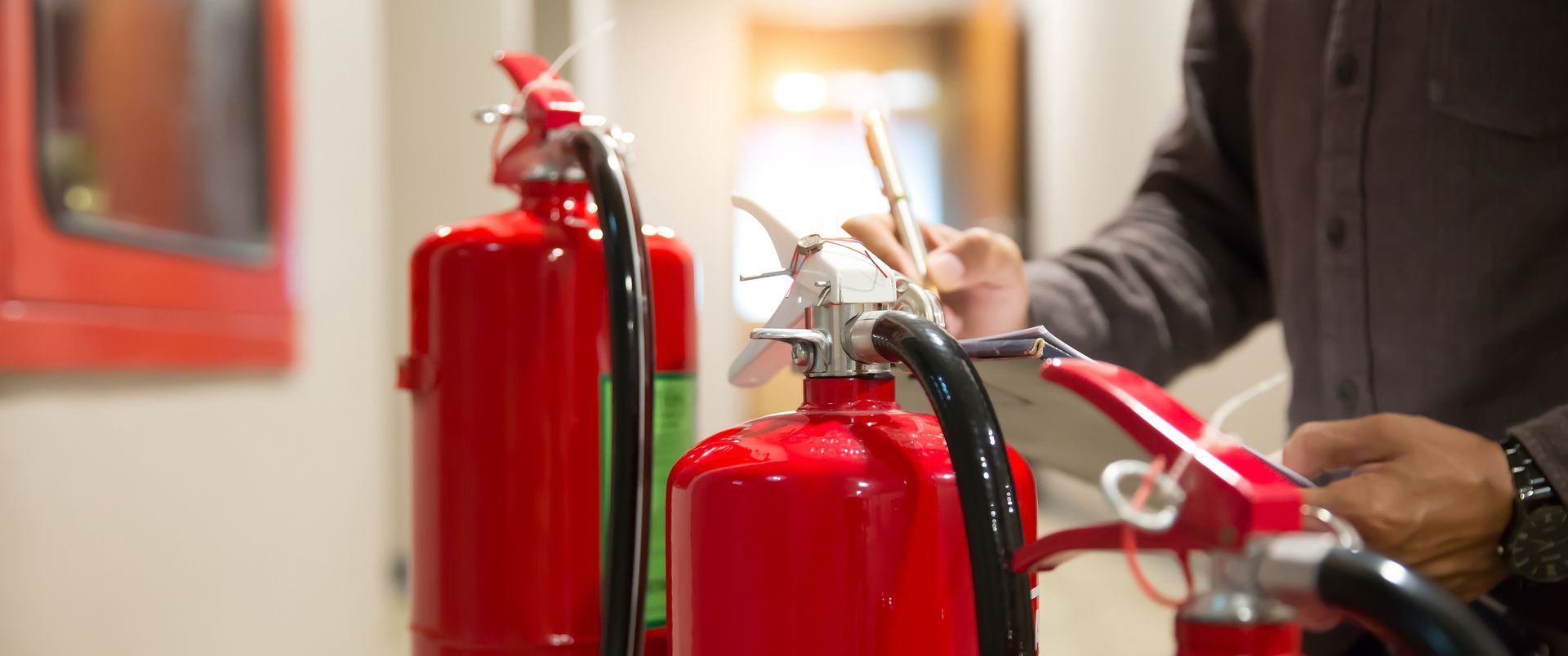 Des extincteurs rouges sont exposés, une personne prend des notes en arrière plan.