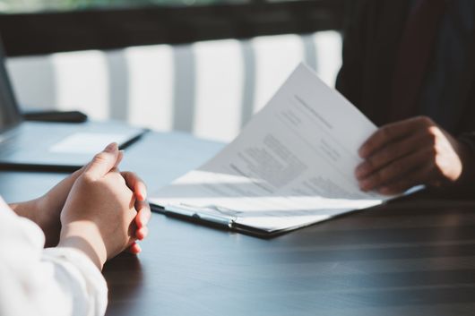 Des mains examinent des documents de part et d'autre d'une table sombre dans un bureau lumineux.