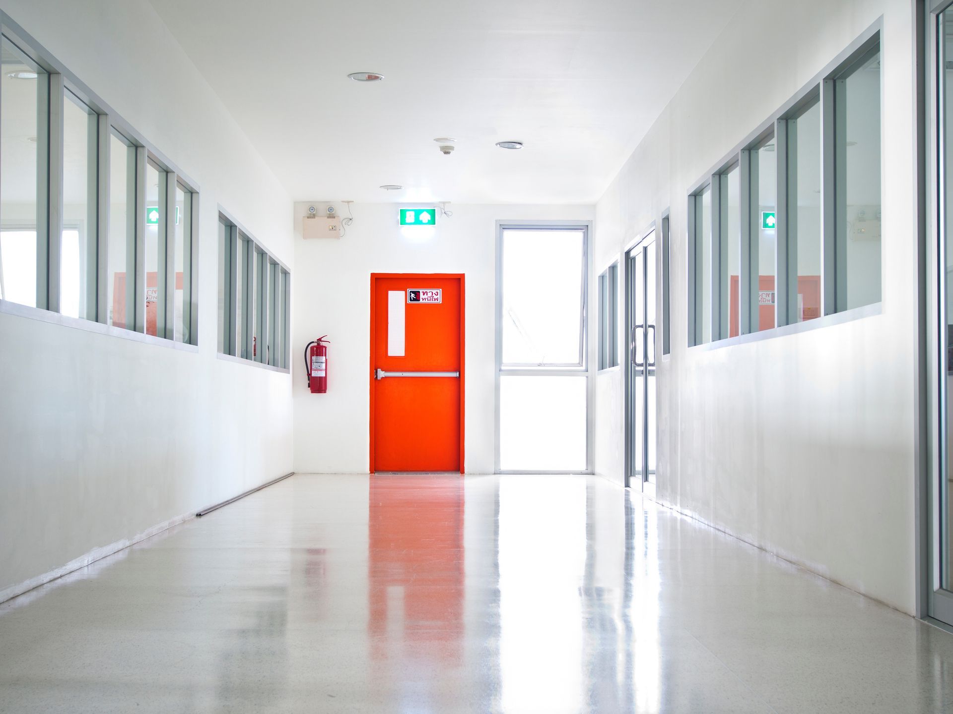 Couloir blanc vide avec une porte orange vif au fond et des fenêtres de chaque côté.