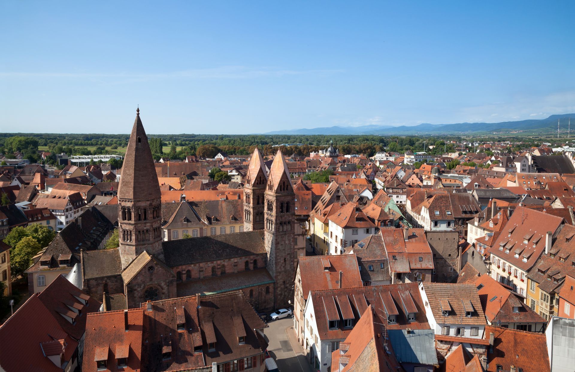 Vue aérienne d'une ville historique aux toits de tuiles rouges et à la grande cathédrale, sous un ciel d'un bleu limpide.