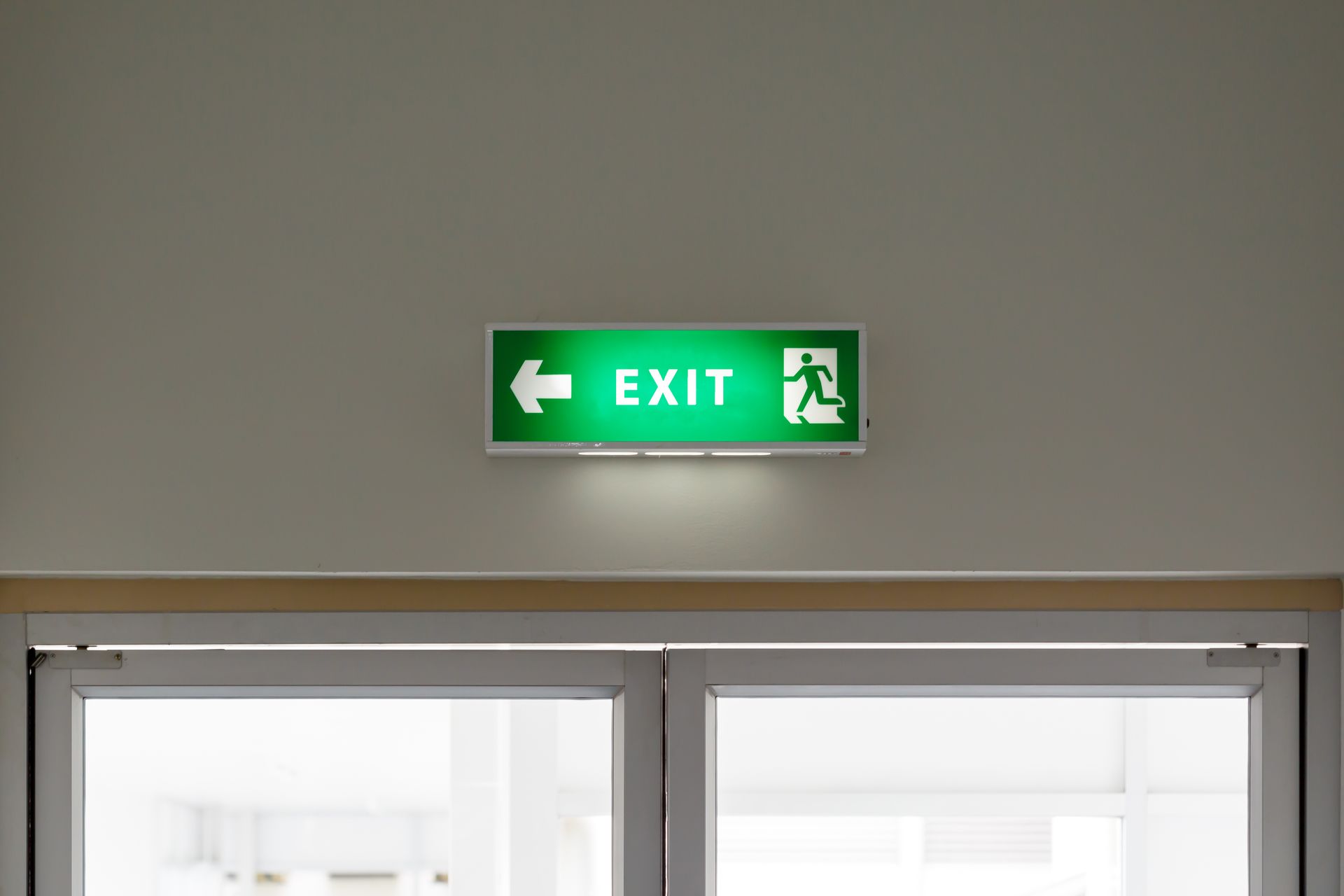 Panneau vert SORTIE au-dessus des portes vitrées d'un couloir.