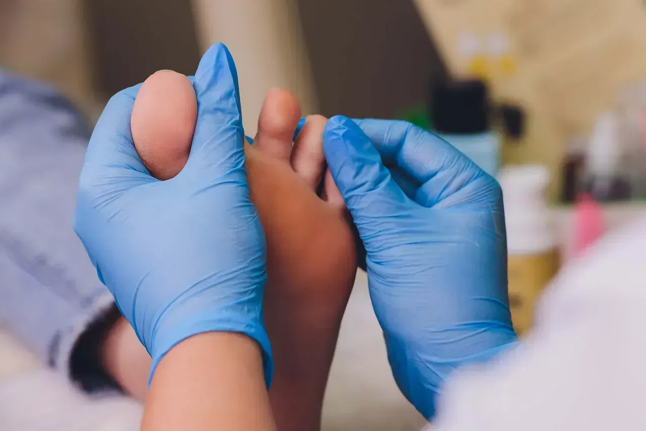 Manos con guantes azules examinando un pie, probablemente en un salón o en un entorno médico.