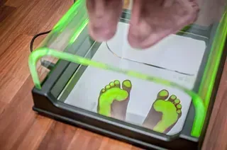 Pies entrando en un escáner de pies. El dispositivo tiene una luz verde que muestra el mapeo de la huella.