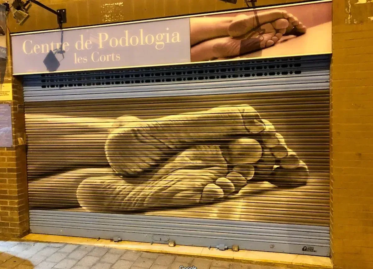 Un escaparate de una clínica de podología con un gran mural de un pie pintado en la puerta de seguridad de metal.