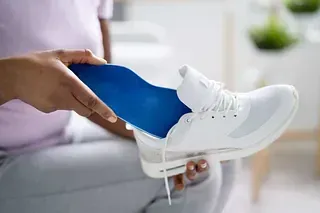 Persona insertando una plantilla ortopédica azul en una zapatilla deportiva blanca.
