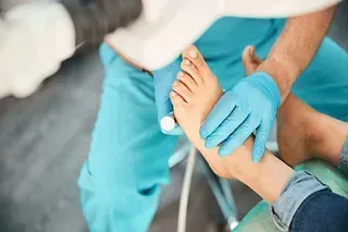 Un podólogo con guantes azules examina el pie de un paciente.