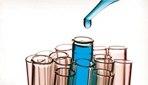 Tubos de ensayo, uno de ellos llenándose con un líquido azul mediante un gotero.