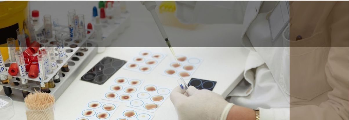 Un técnico de laboratorio con guantes y bata blanca, trabajando con muestras de sangre.