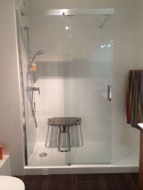 Cabine de douche en verre avec siège rabattable, douchette et serviette sur le mur de droite