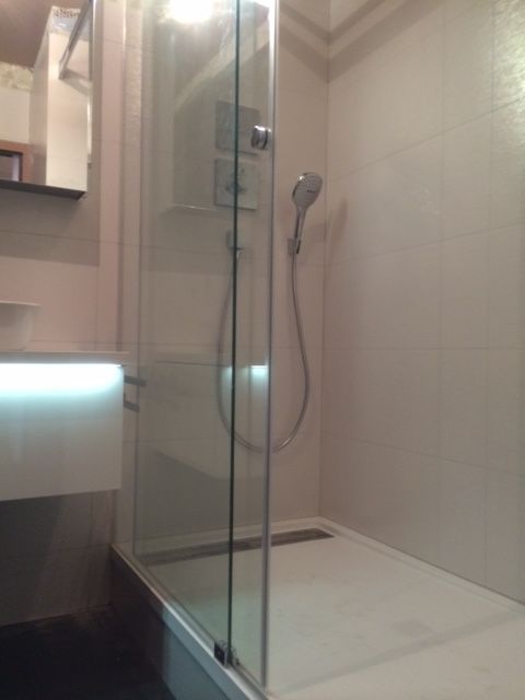 Douche moderne avec porte en verre transparent, murs carrelés et pommeau de douche à main.