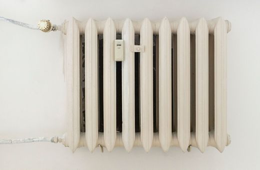 Radiateur mural blanc avec ailettes verticales et tuyaux apparents sur un mur blanc