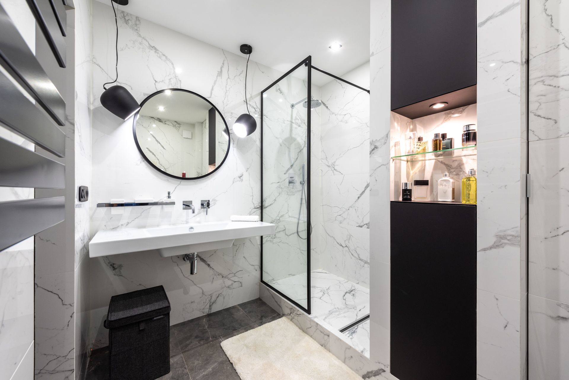 Salle de bains moderne carrelée en marbre avec lavabo mural, miroir rond, douche et touches de noir.