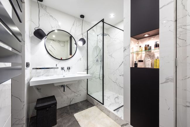 Salle de bains moderne carrelée en marbre avec lavabo mural, miroir rond, douche et touches de noir.