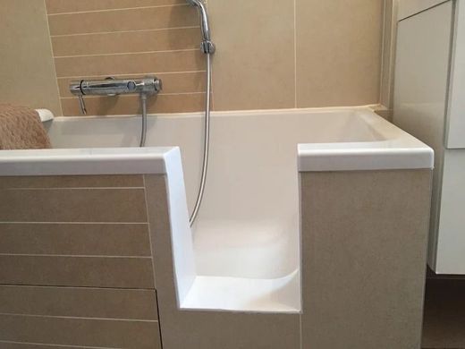Baignoire à porte accessible avec siège intégré et douchette dans une salle de bain carrelée