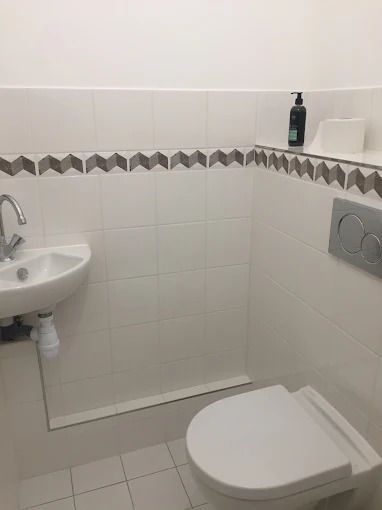 Petite salle de bains avec toilettes, lavabo mural et murs carrelés avec une frise décorative.