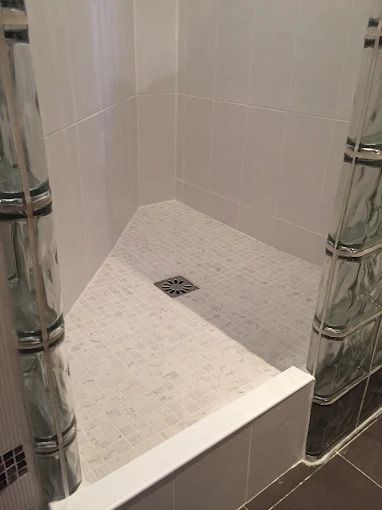 Cabine de douche carrelée blanche avec barres d'appui chromées et petite bonde carrée au sol