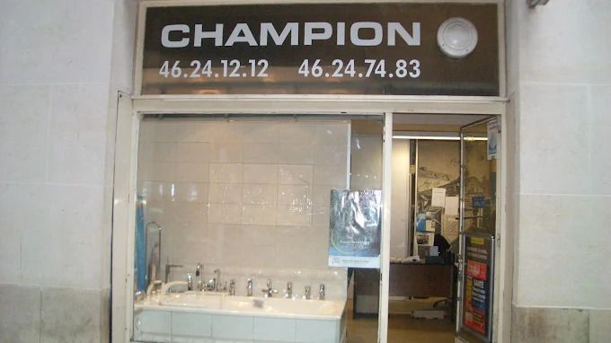 Devanture de magasin avec une enseigne noire CHAMPION au-dessus d'une vitrine et d'une porte coulissante.