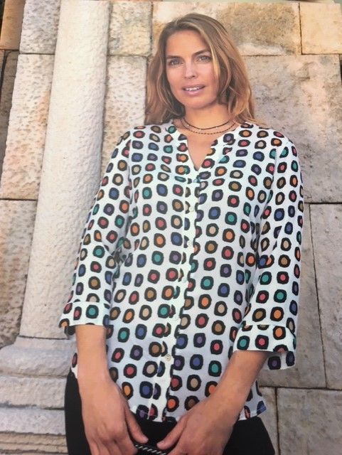 Una mujer que lleva una camisa de lunares está parada frente a un muro de piedra.