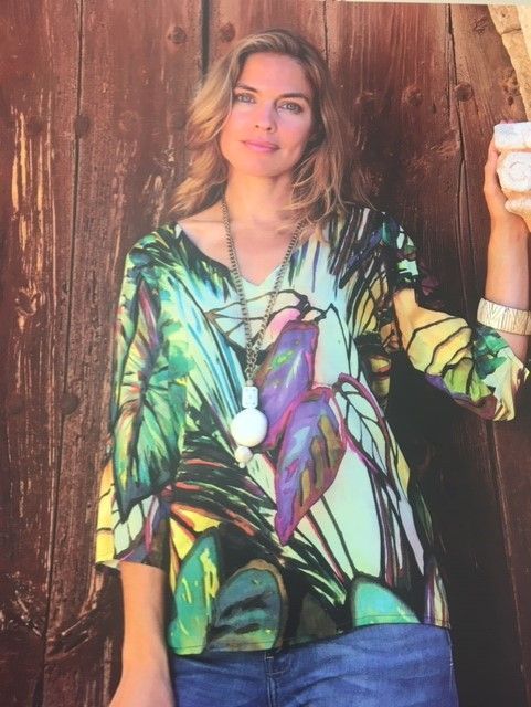 Una mujer que lleva una camisa colorida y un collar está parada frente a una pared de madera.