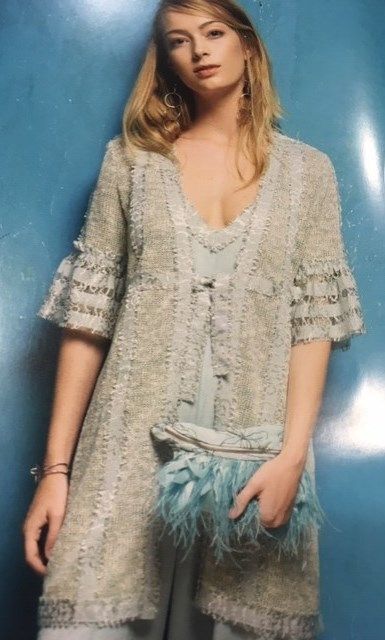 Una mujer está parada frente a una pared azul, vistiendo un suéter y un bolso de mano de plumas.