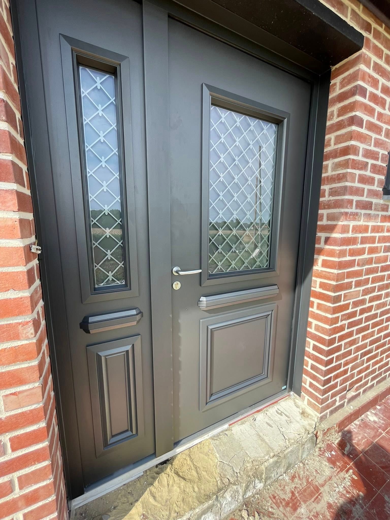 Porte double gris foncé avec panneaux de verre à motif losange, façade en briques.