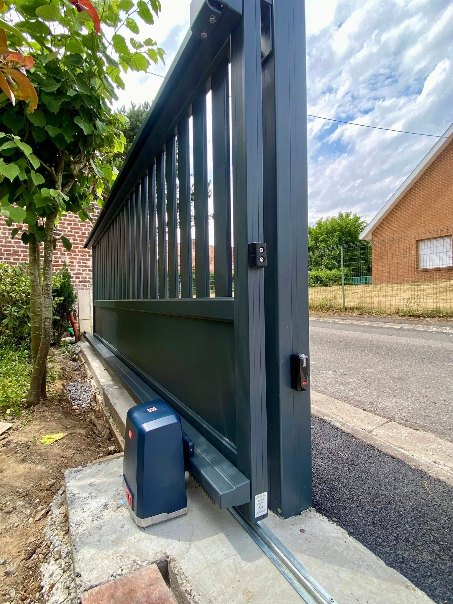 Portail coulissant gris avec moteur automatisé sur socle en béton, partiellement ouvert sur rue.
