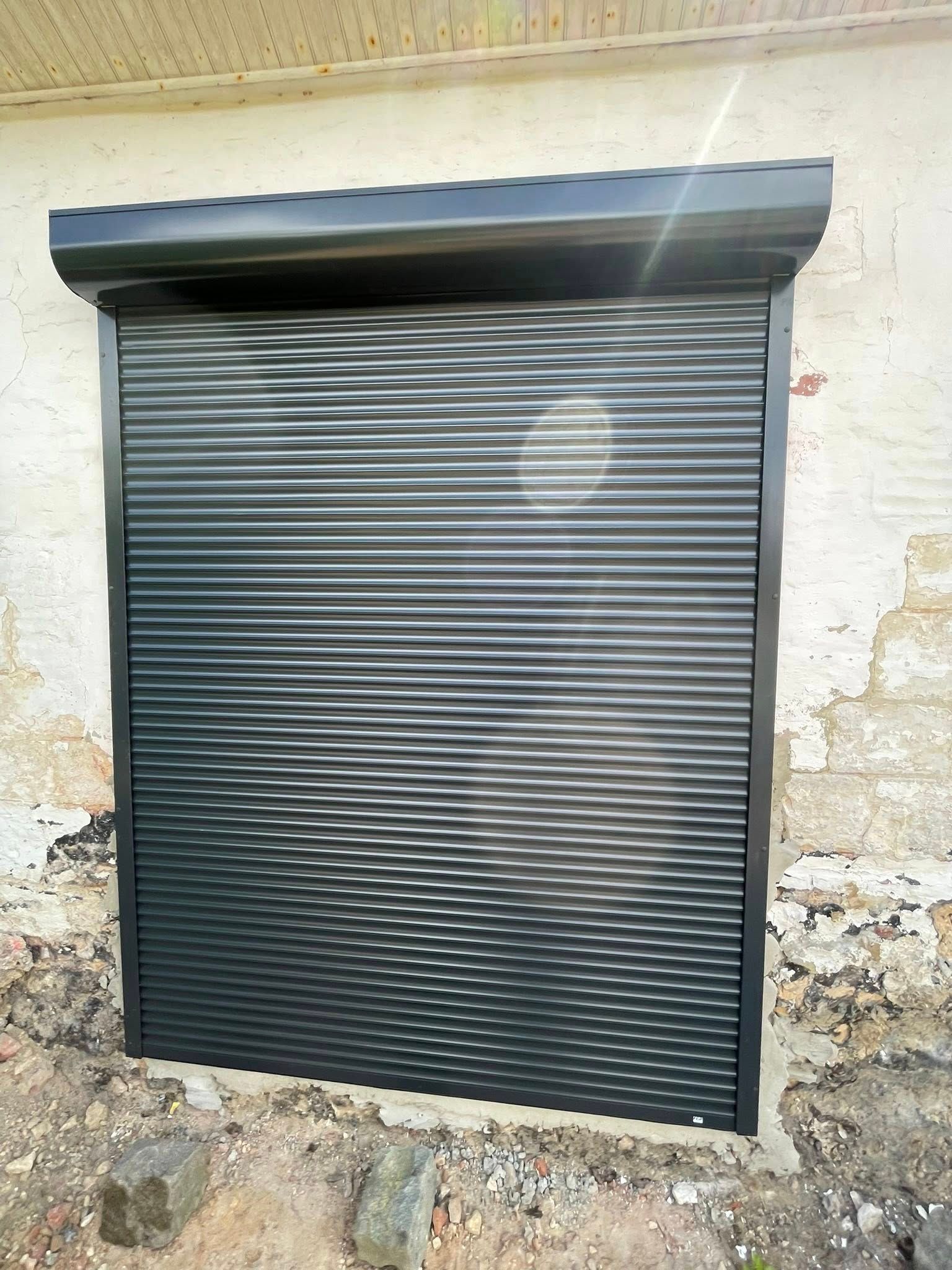Volet roulant gris foncé installé sur un mur de briques claires et patinées par le temps.