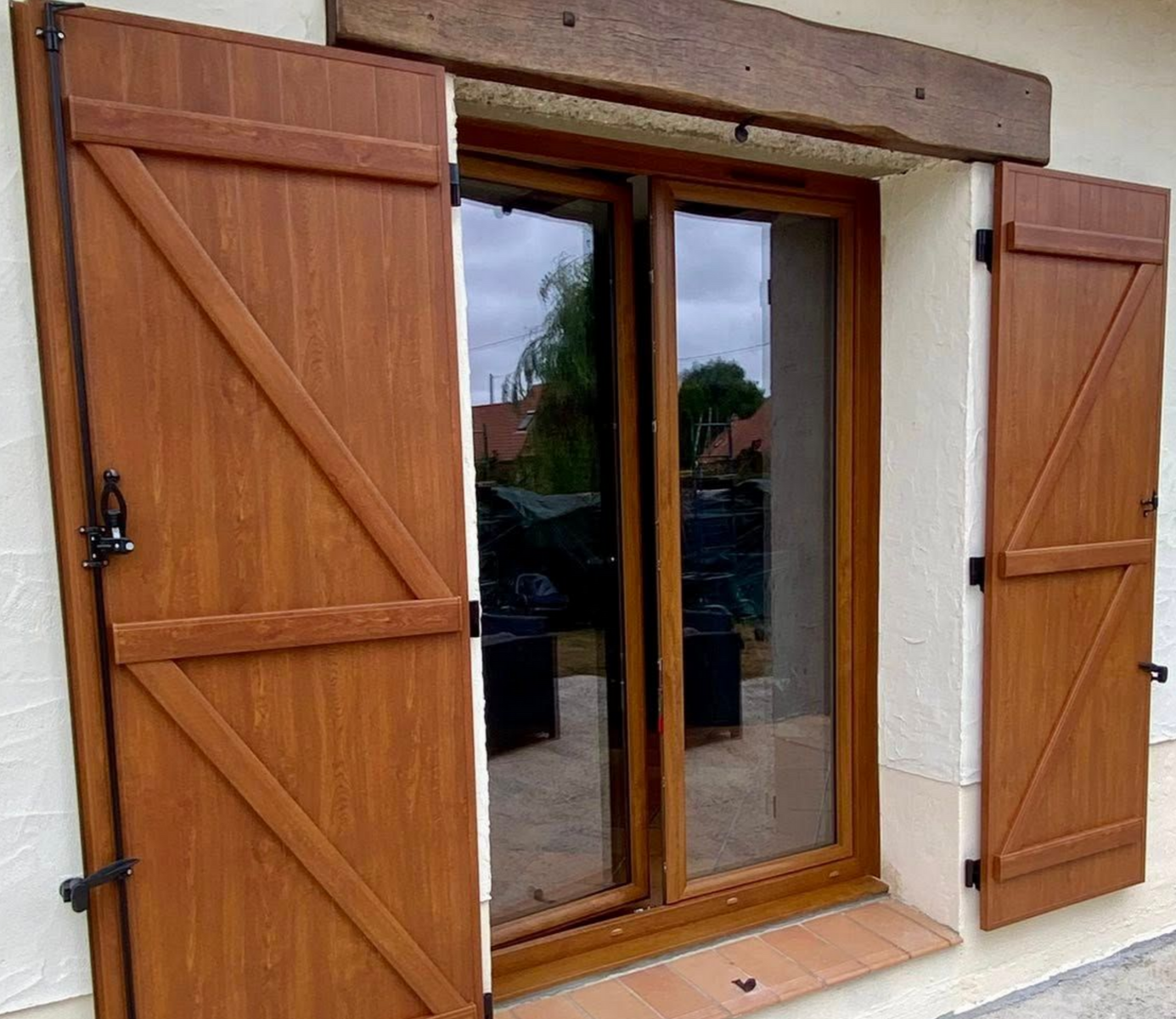 Des volets bruns s'ouvrent sur une fenêtre laissant se refléter un paysage extérieur.