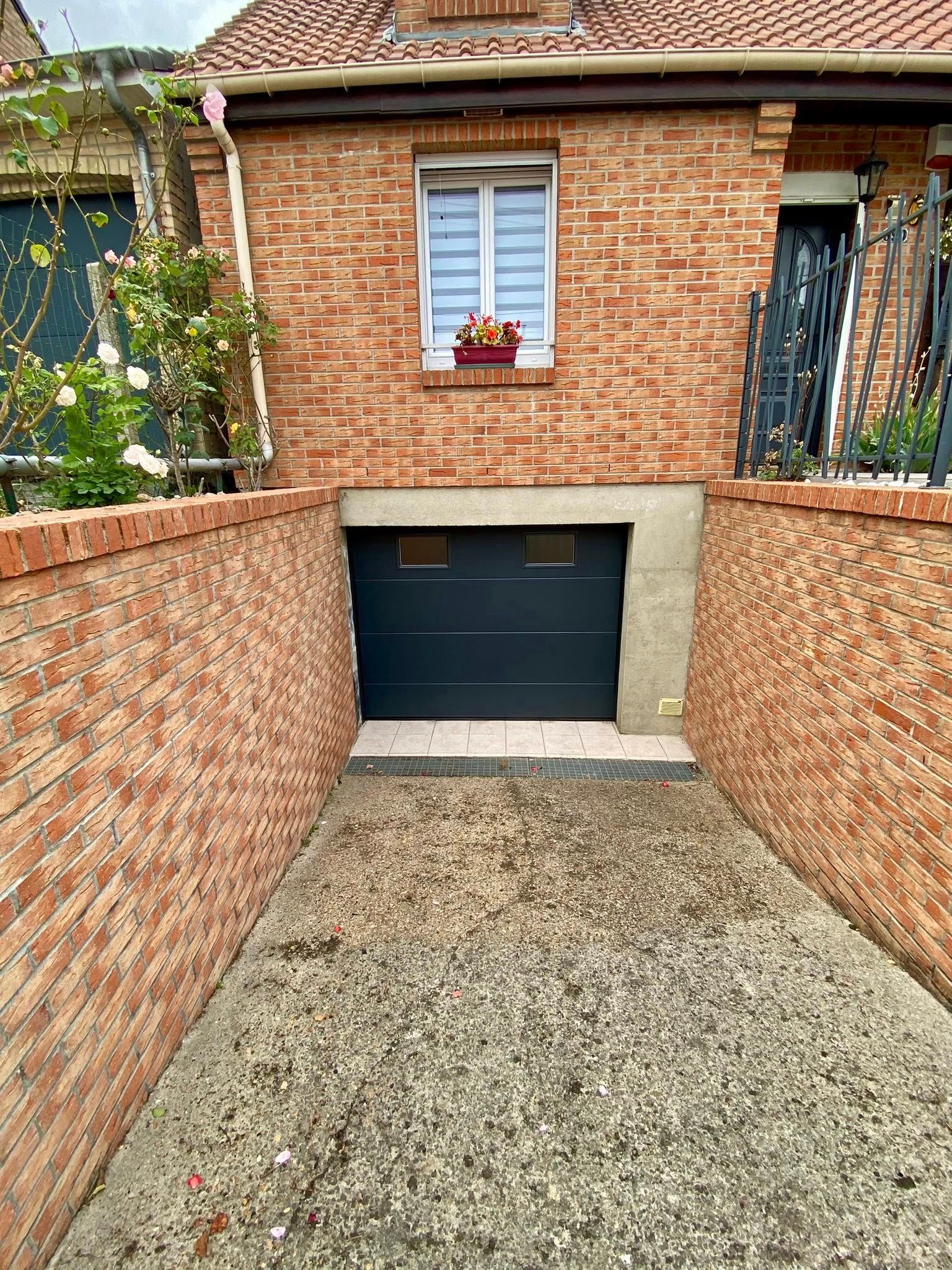 Bâtiment en briques avec une porte de garage sombre encastrée dans la maçonnerie. Allée de gravier menant au garage.