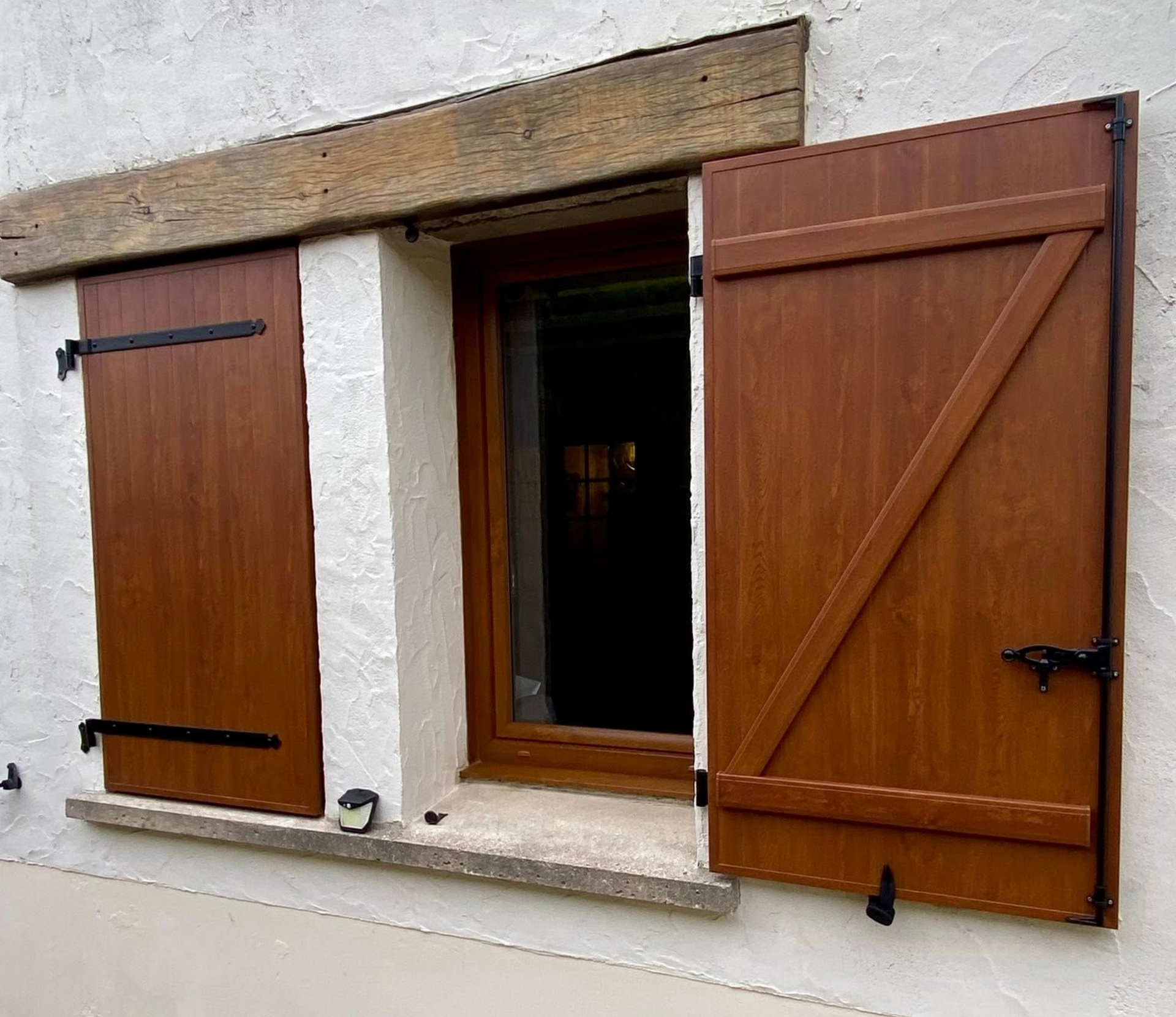 Volets bruns sur une fenêtre à cadre et poutre en bois. Un volet ouvert.