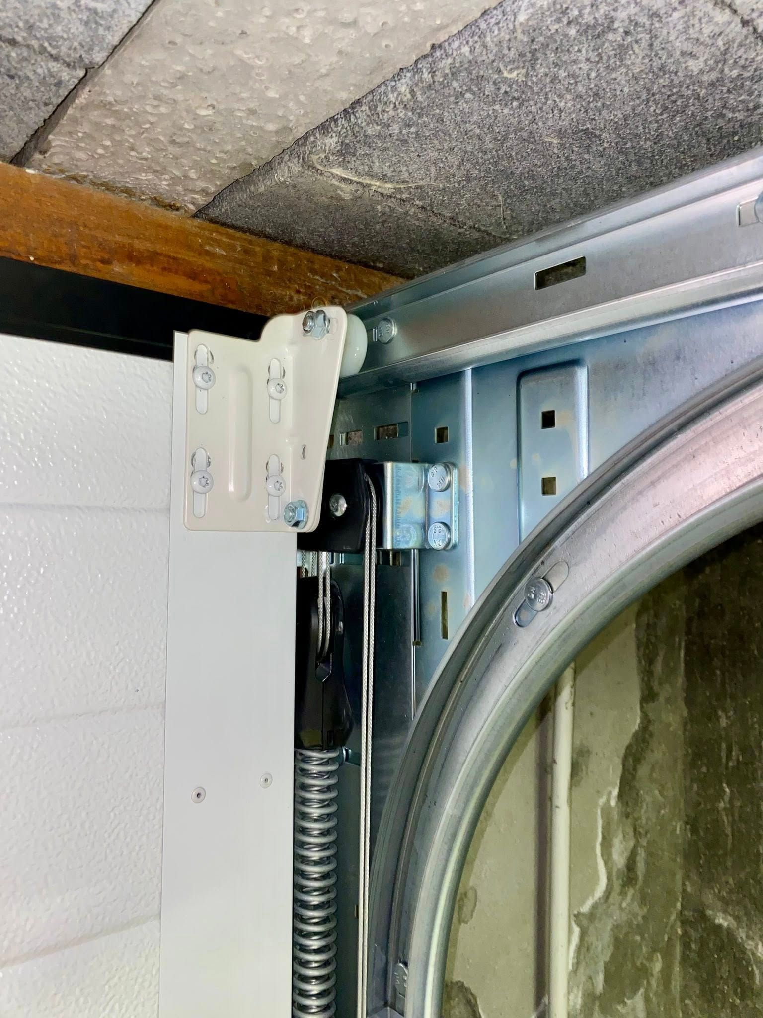 Gros plan sur le rail et les ferrures de porte de garage, y compris le rail, le rouleau, le ressort et le support de montage.