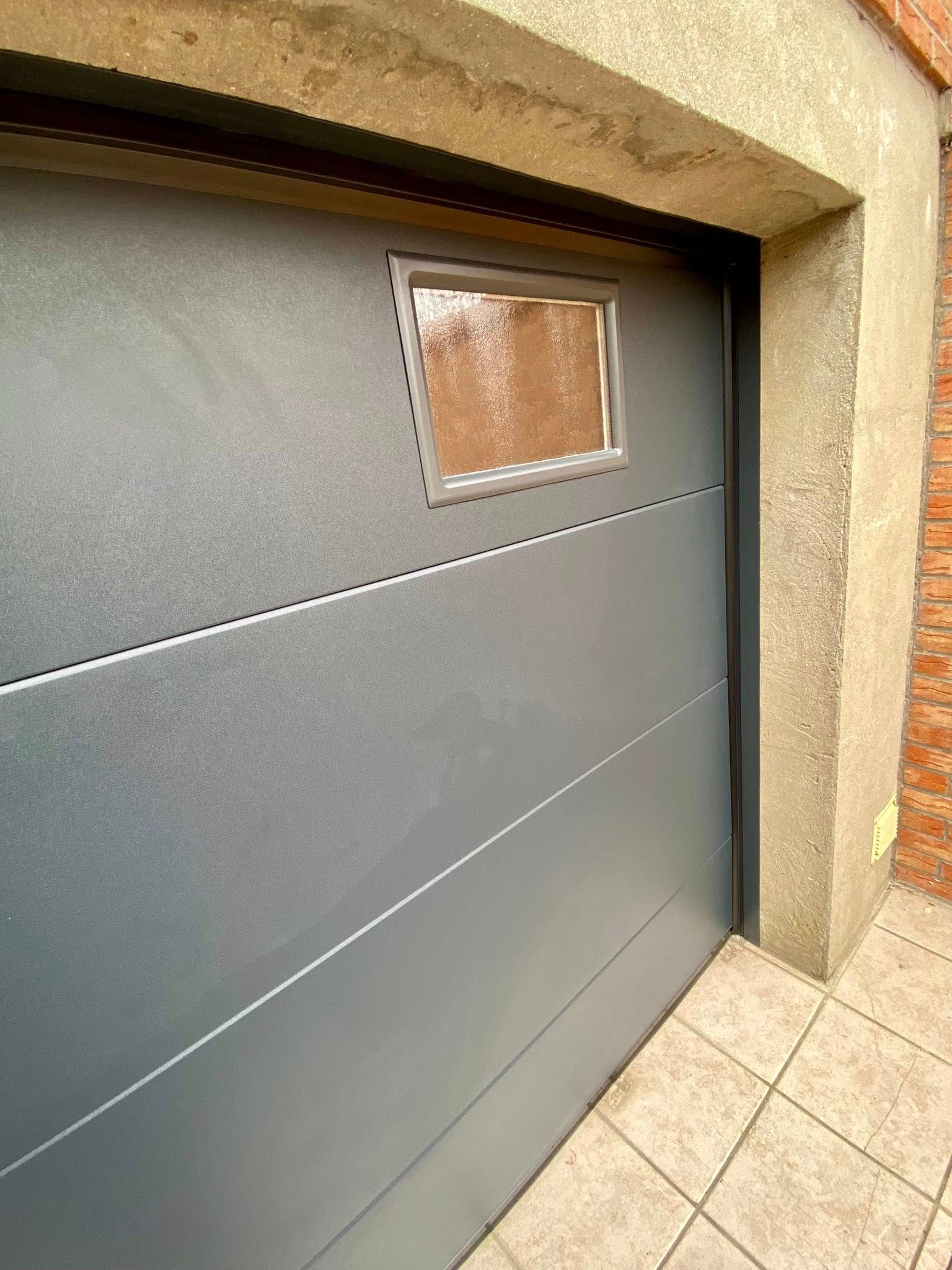 Porte de garage grise avec petite fenêtre.