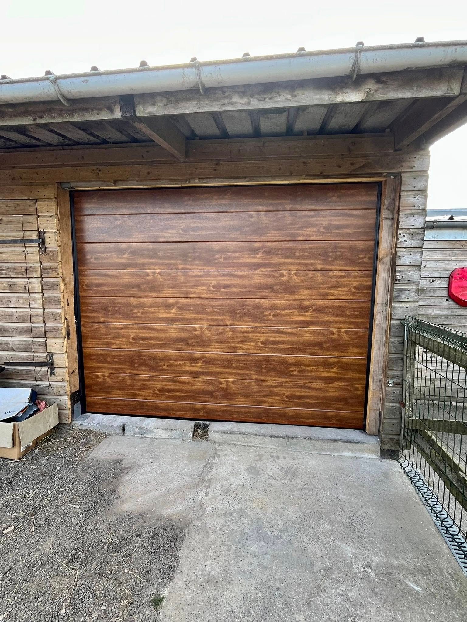 Porte de garage marron avec une texture de grain de bois, intégrée à un bâtiment en bois.
