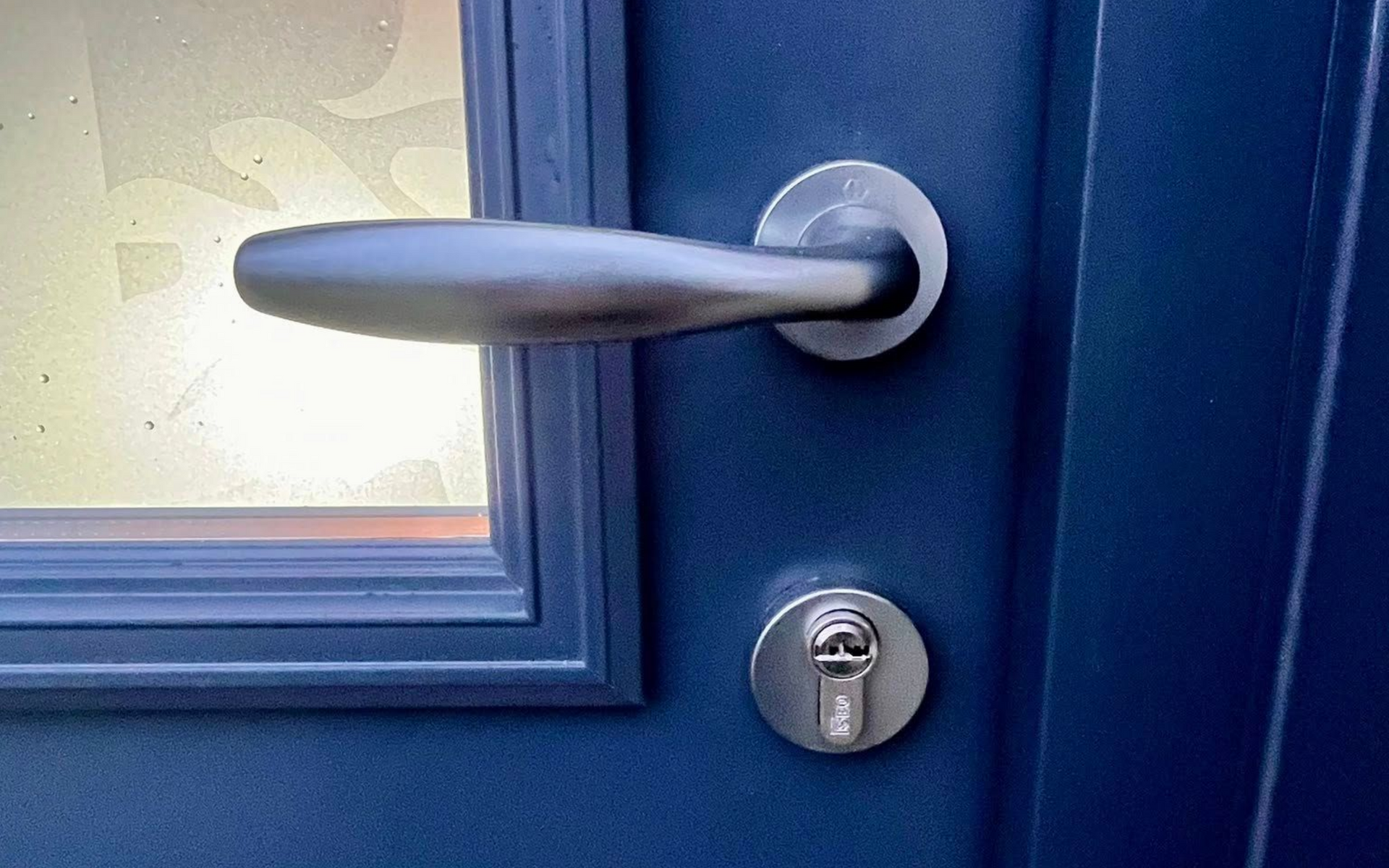 Porte bleue avec poignée et serrure argentées. Fenêtre visible sur la gauche.