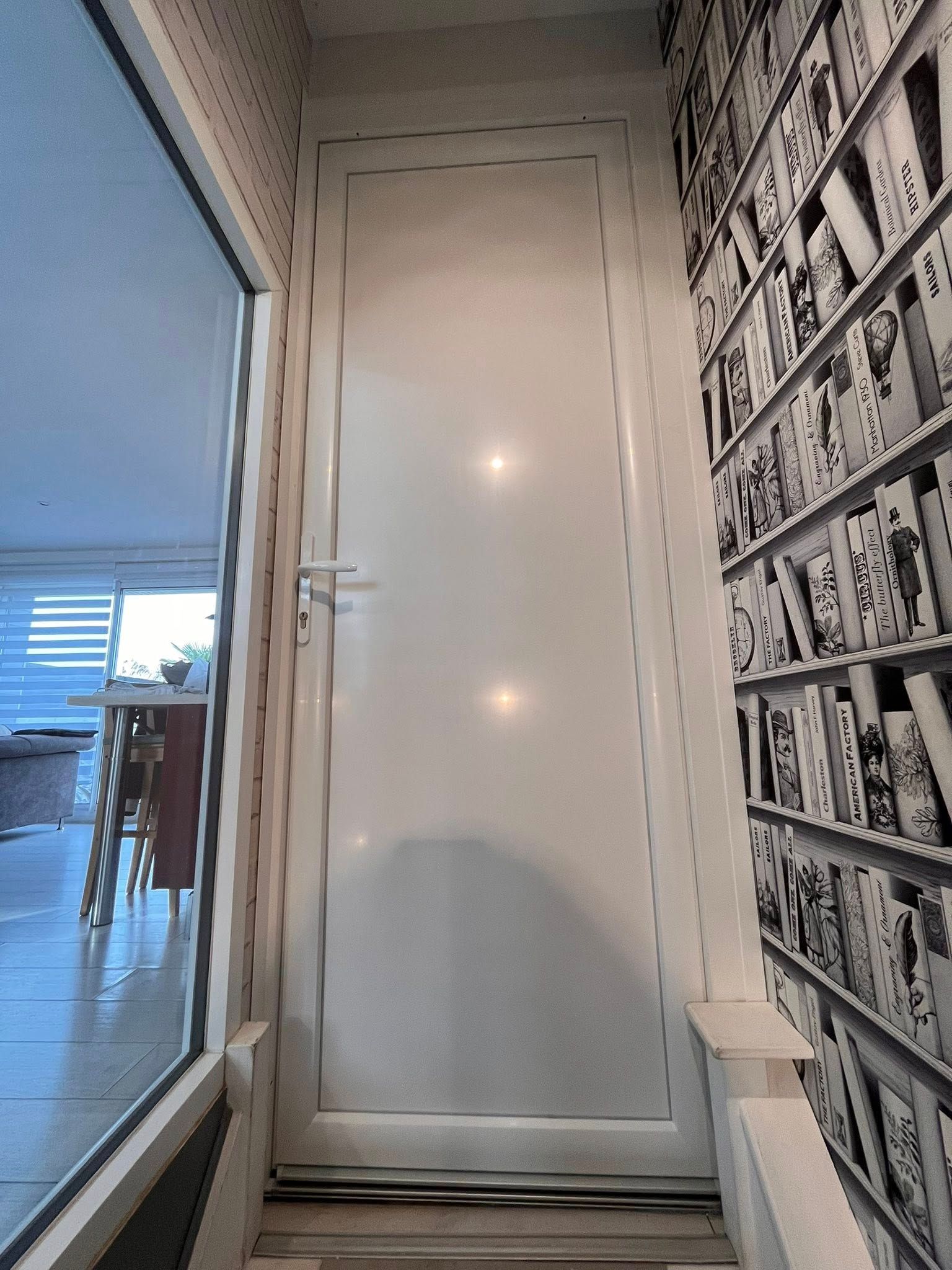 Porte blanche dans un couloir avec une grande fenêtre à gauche et du papier peint à motifs de cartes à jouer à droite.