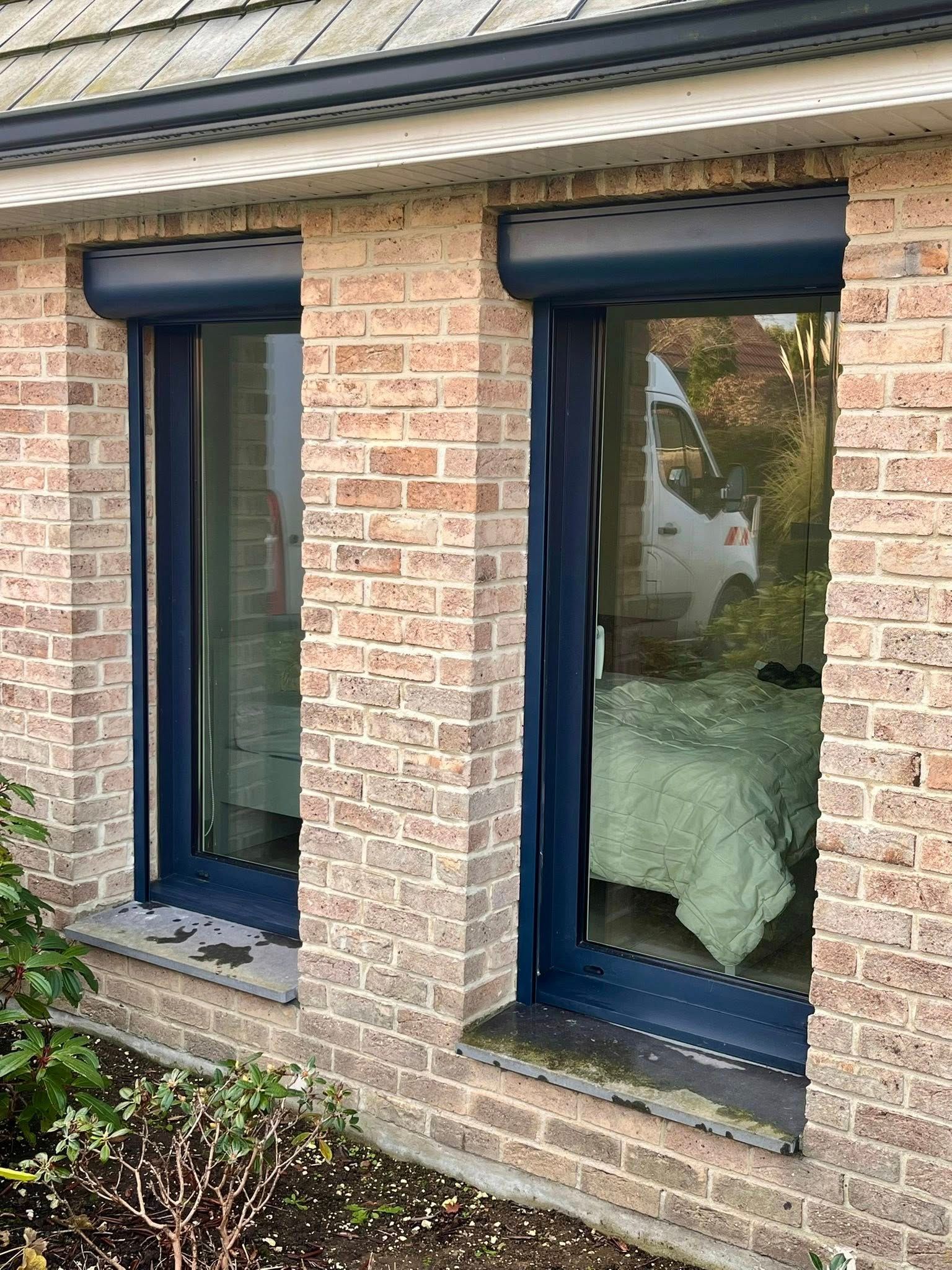Deux fenêtres aux volets bleus fermés sur un bâtiment en briques, vue extérieure.