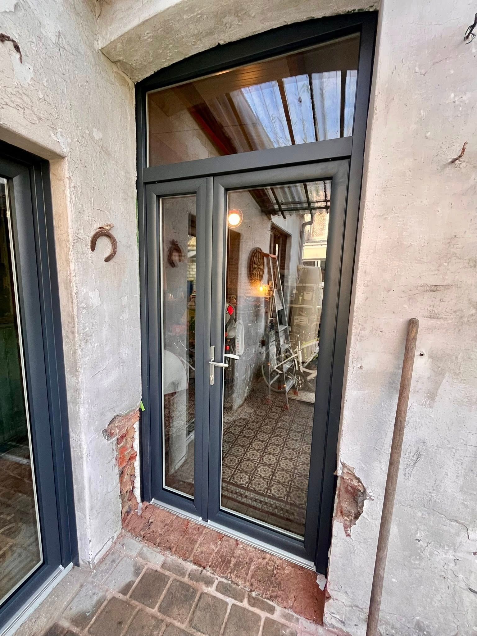 Portes doubles vitrées à cadres gris foncé, encastrées dans une entrée en briques et en pierres patinées.